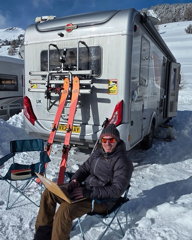 Darren working from a laptop beside the motorhome at an alpine ski resort